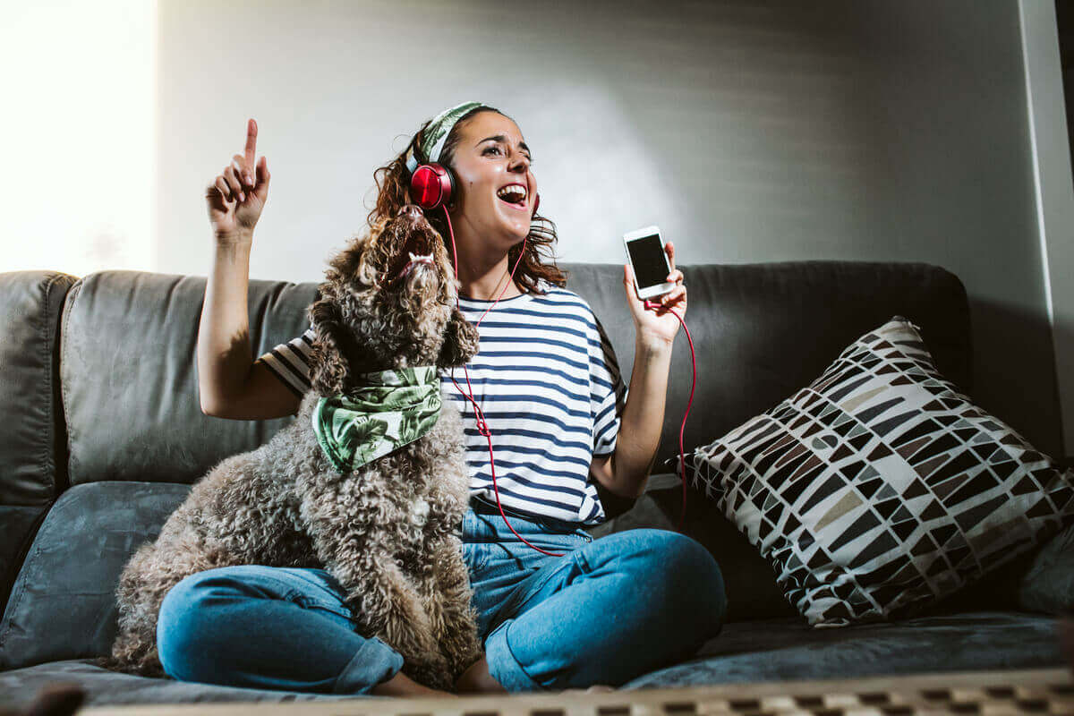 En kvinne som sitter på sofaen og lytter til musikk med hunden sin