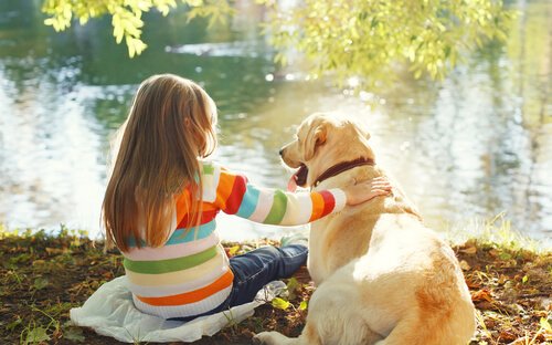 En flicka som sitter med sin hund vid en flod