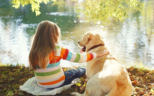 A girl sitting with her dog next to a river