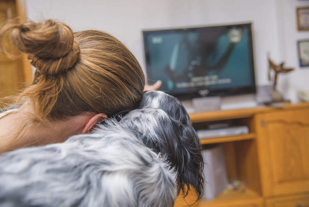 A woman watching TV with her dog.