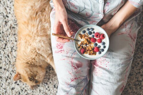 A woman eating her cereal with her cat.