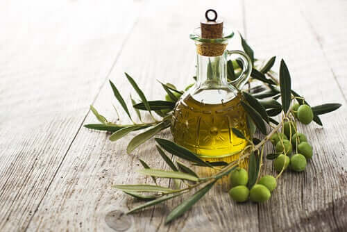 A bottle of olive oil sitting on a table with olive leaves and olives. 
