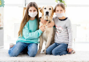 Girls wearing masks hugging a dog.