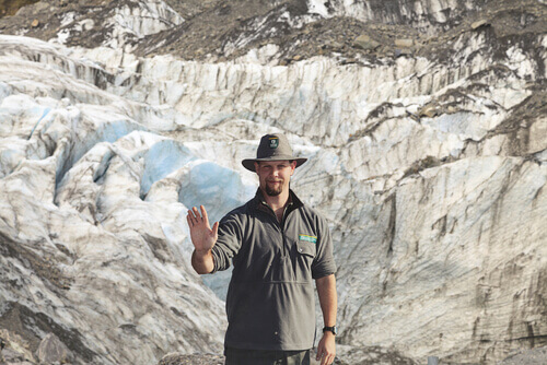 A park ranger waving with a mountain in the background.