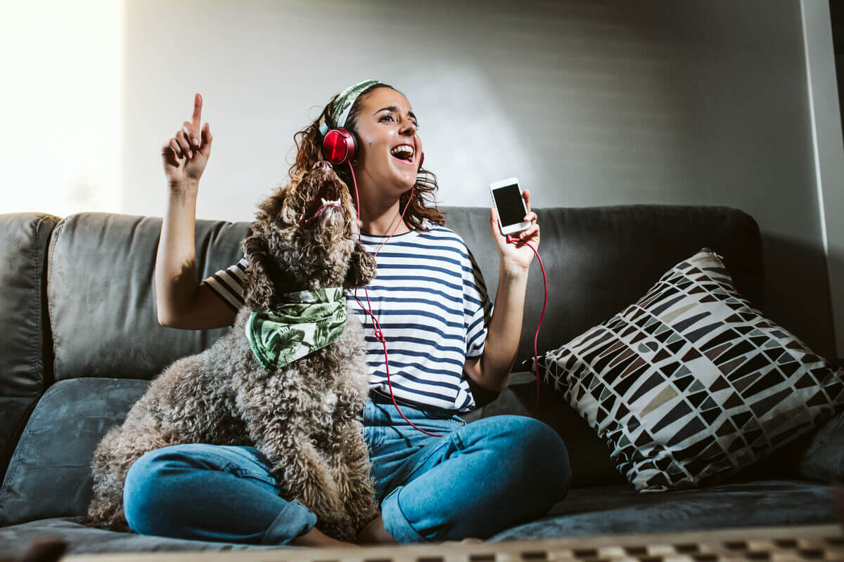 A woman sitting on the couch listening to music with her dog.